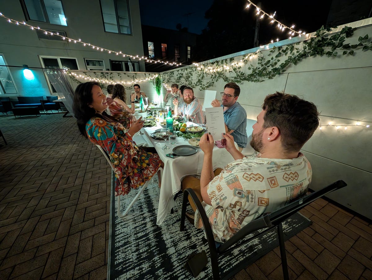 A group of people sitting around a table outside at night.