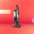 Black Shark brand Navigator Swivel Pro Plus corded upright vacuum on an orange and pink gradient background