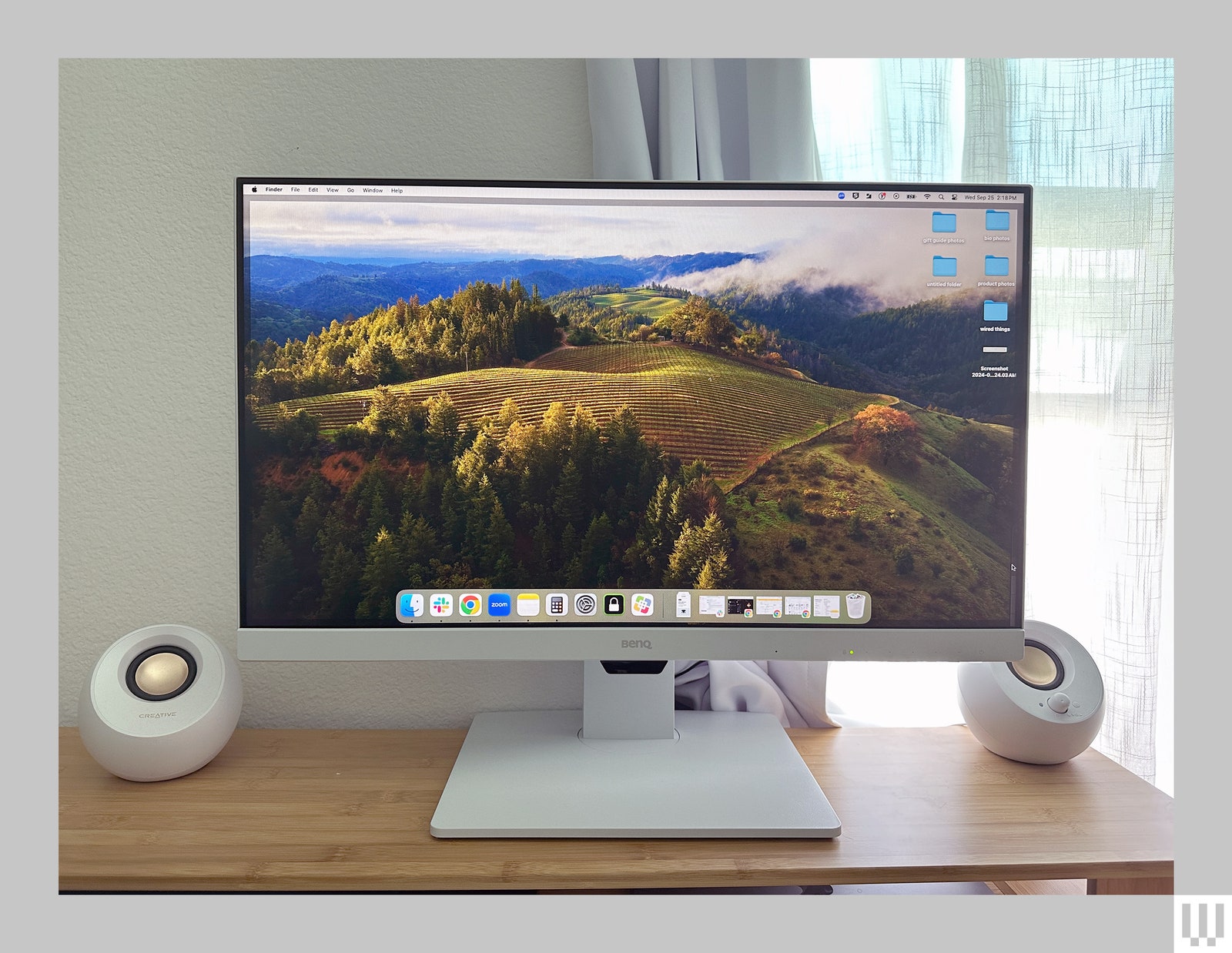 BenQ monitor a slim white computer screen with a square base sitting on a wooden table with a spherical shaped speaker...