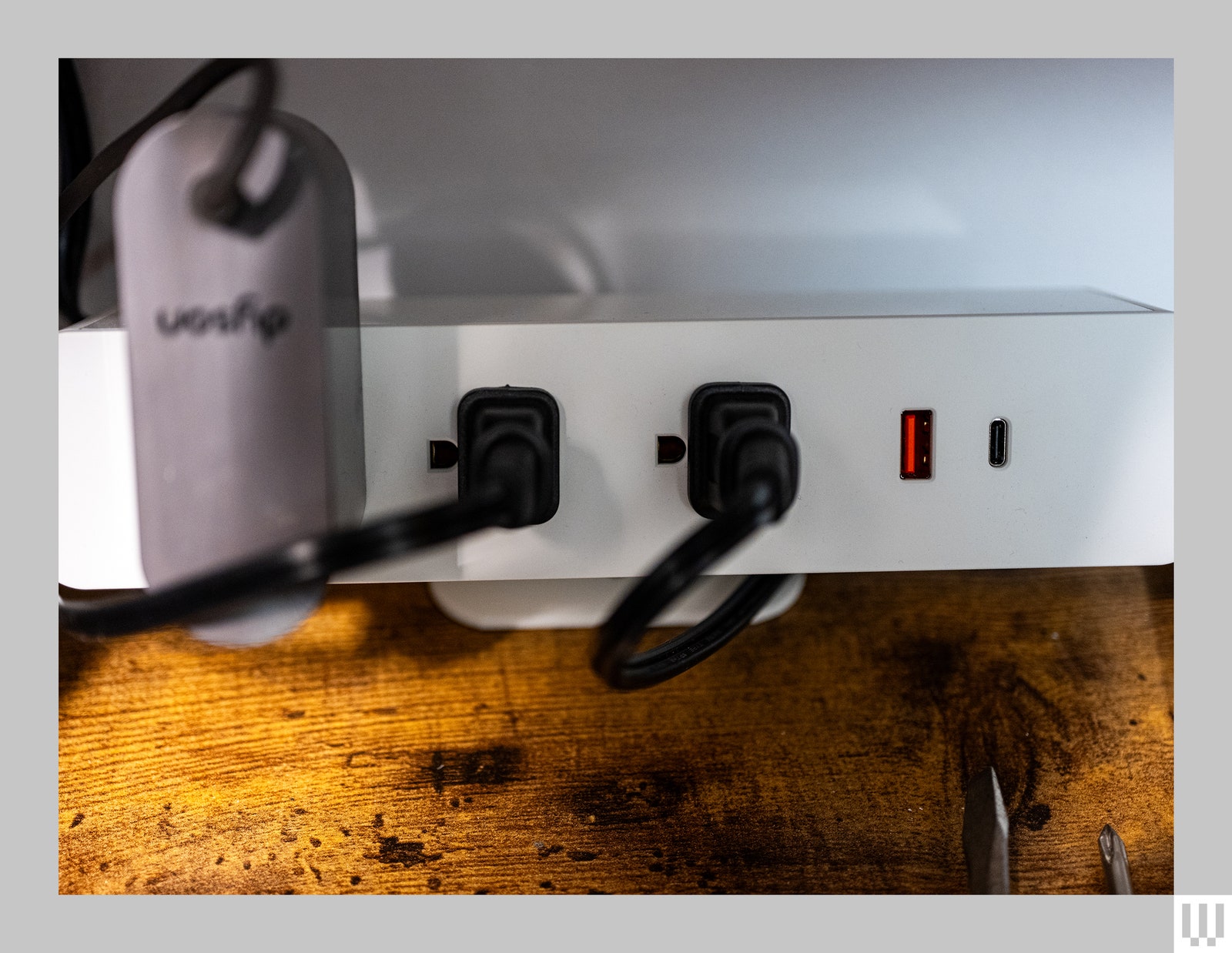 Front view of Branch Clamp On a white electrical power strip gripping the edge of a wooden desk