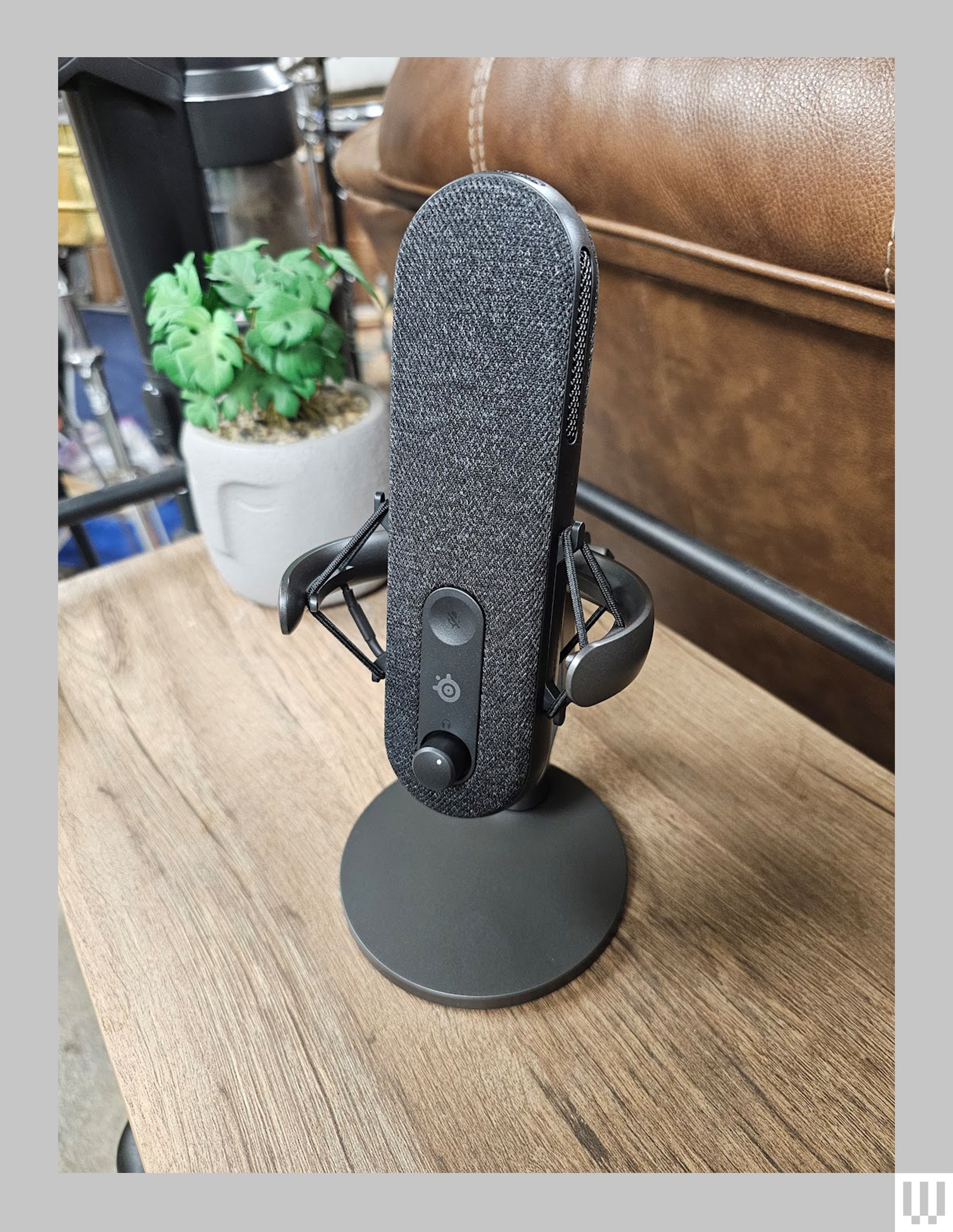 The ovalshaped SteelSeries Alias microphone on a circular stand with mesh cover over the front sitting on a small wooden...