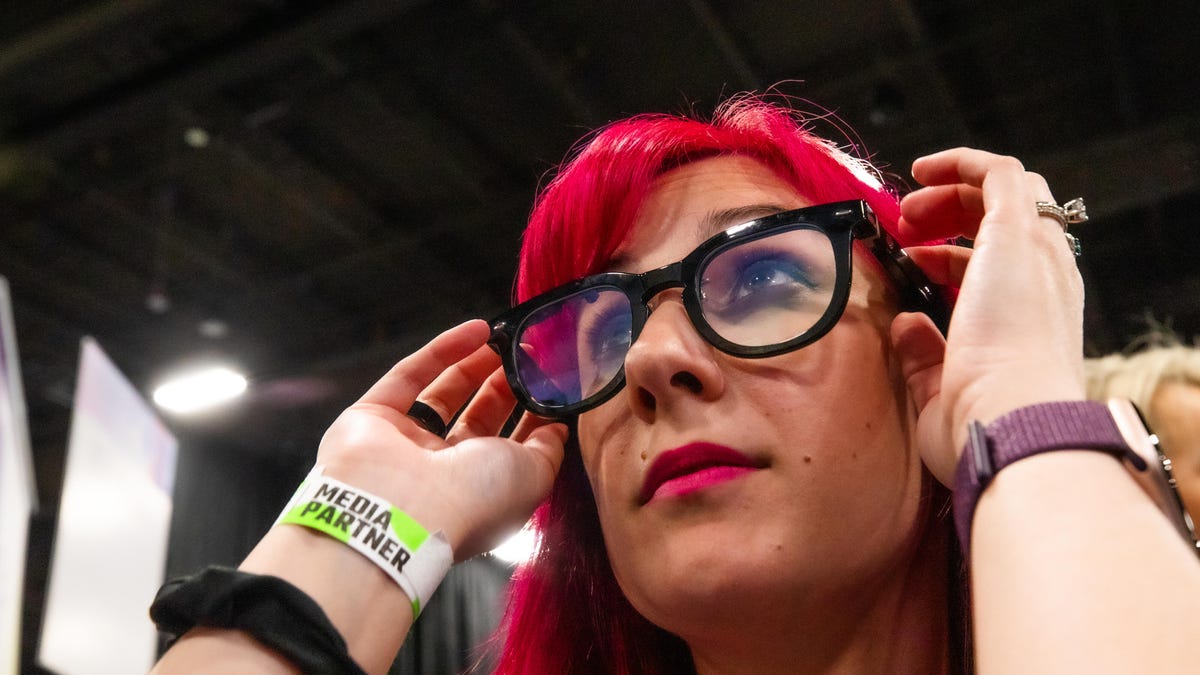 A woman with red hair adjusts a pair of black framed glasses