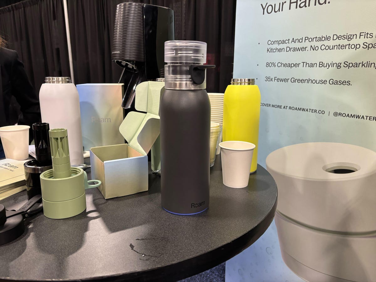 A black stainless steel water bottle sits on a table with cups.