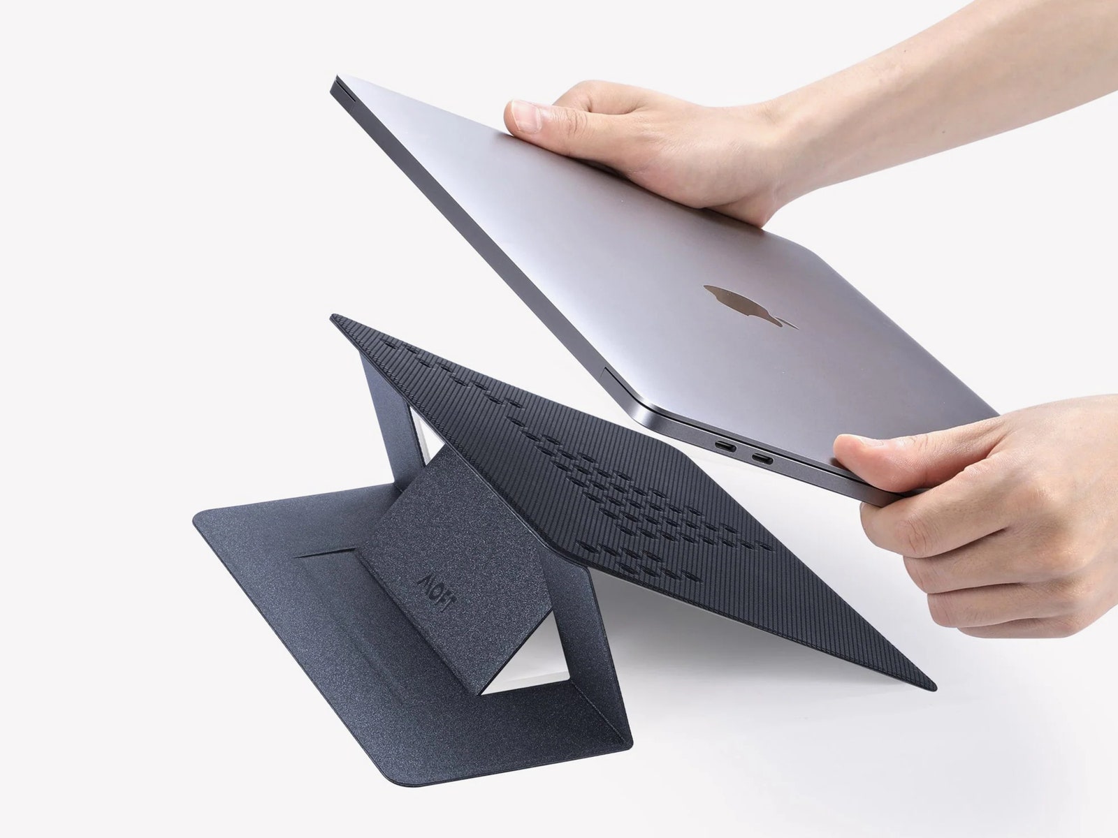 Moft Invisible Stand a black angular laptop stand with two hands holding a silver laptop about to place it on top