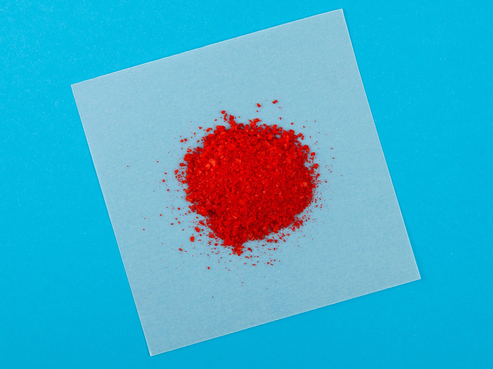 Small pile of red powder on a piece of parchment paper with a solid blue blackground