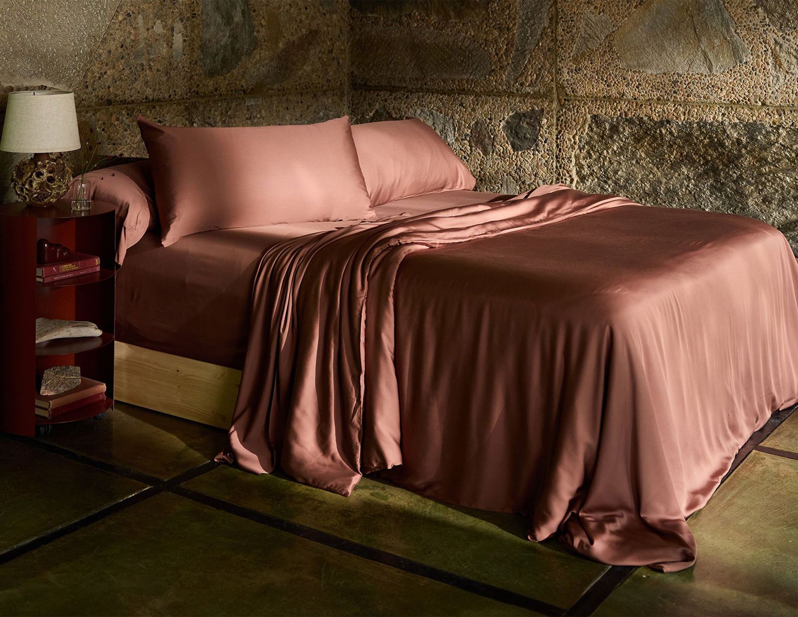 Brownish red colored sheets and pillowcases on a bed in a room with stone walls