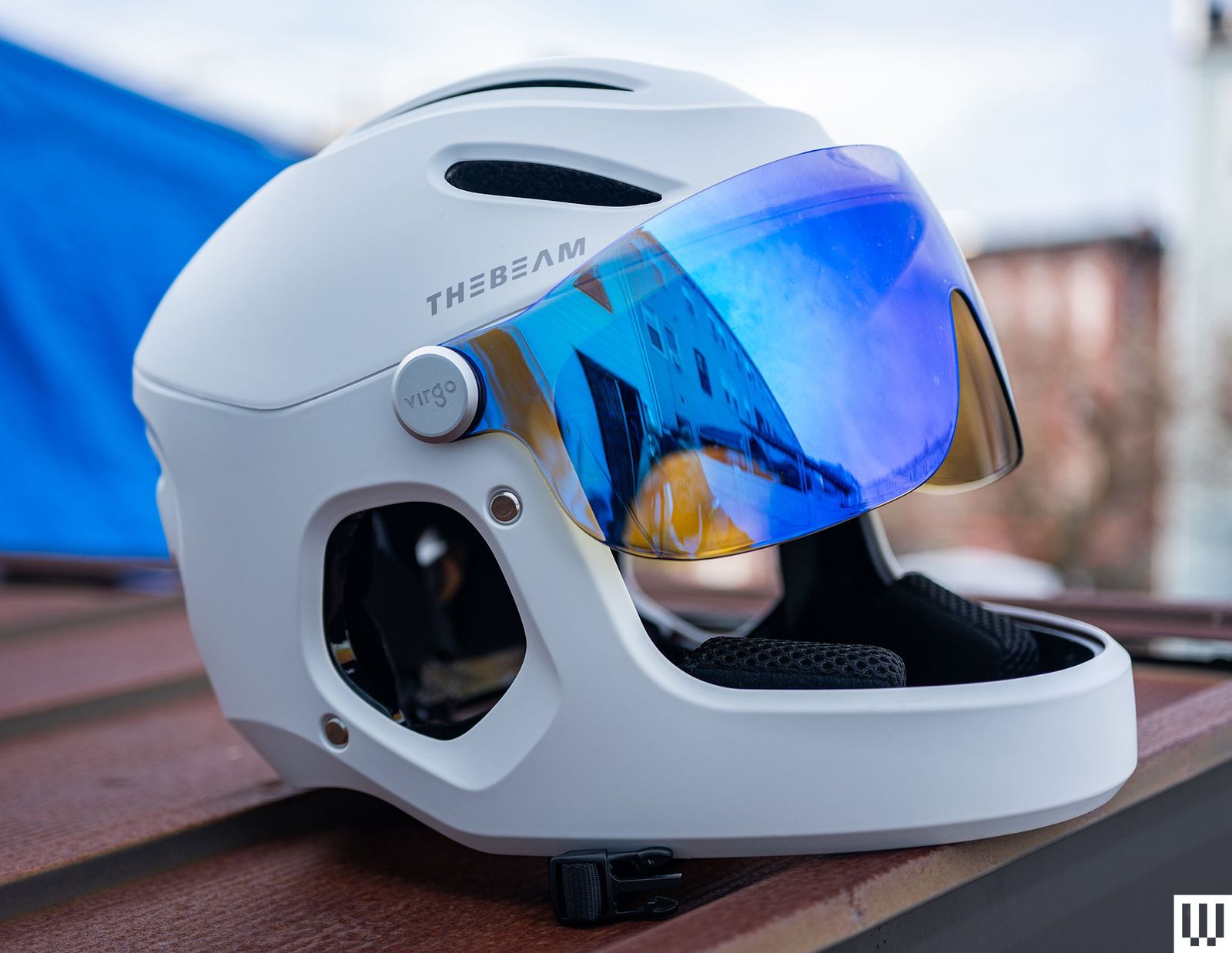 The Beam Virgo a white helmet with blue reflective lenses sitting on a wooden surface