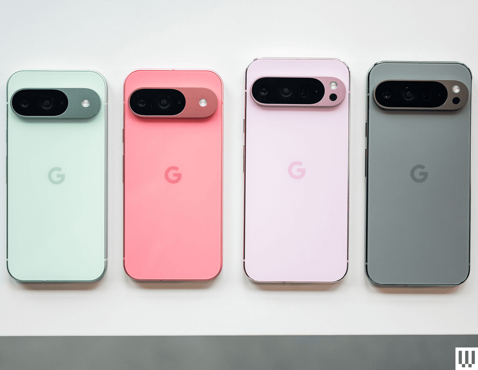 4 mobile phones face down camera side up side by side in teal pink light pink and grey .