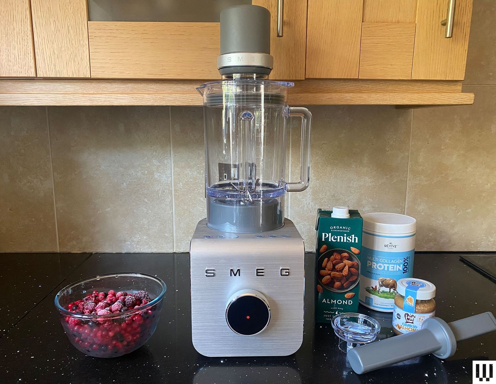 Blender with large steel grey base clear container and additional attachment on top sitting on a black container with...