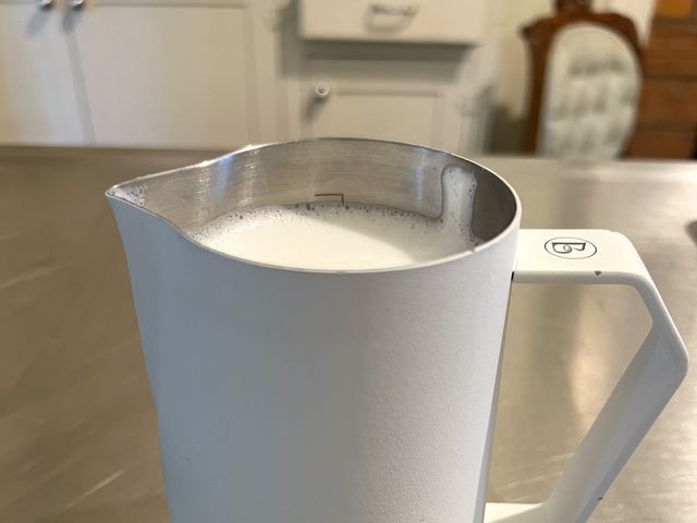 Brewista Frothing Pitcher, a white canister with angled handle on metallic kitchen counter