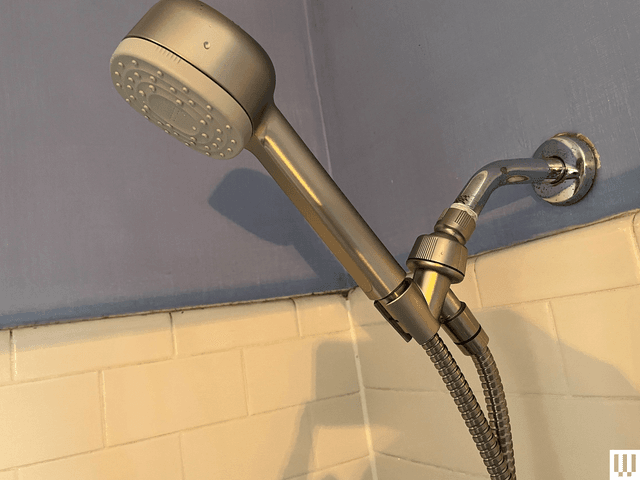 Silver square-shaped showerhead, turned on, with white tiles and blue walls in the background