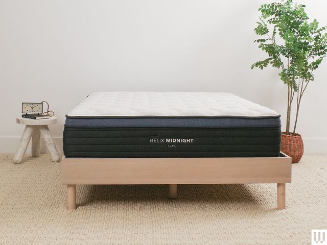 Helix Sleep Midnight Luxe, a white mattress with blue trim, on a minimalist wooden frame with a nightstand and potted plant on either side