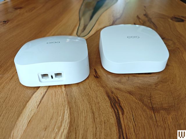 Eero 6 Mesh System, 2 rectangular white devices on a wooden table, one facing front and the other backwards showing the ports