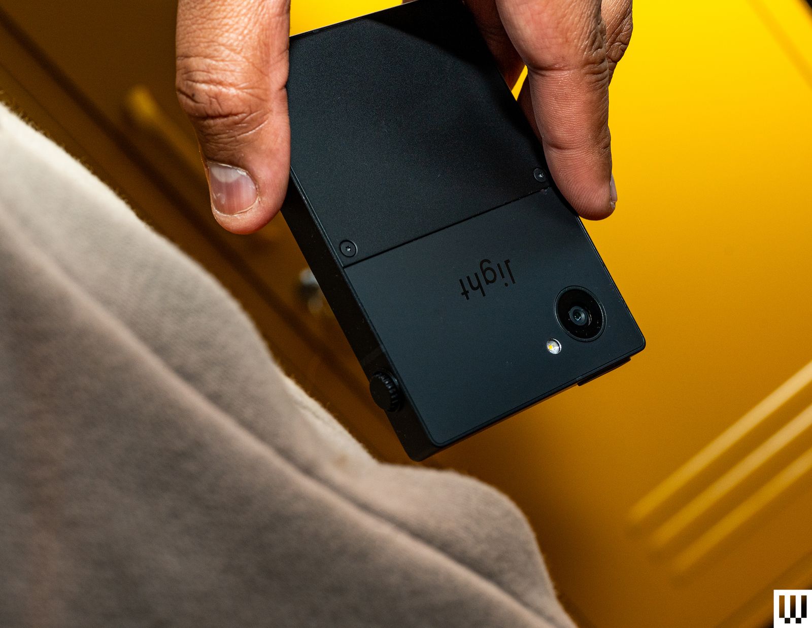 Hand holding a Light Phone III a small black squareshaped device being pulled from a side pants pocket