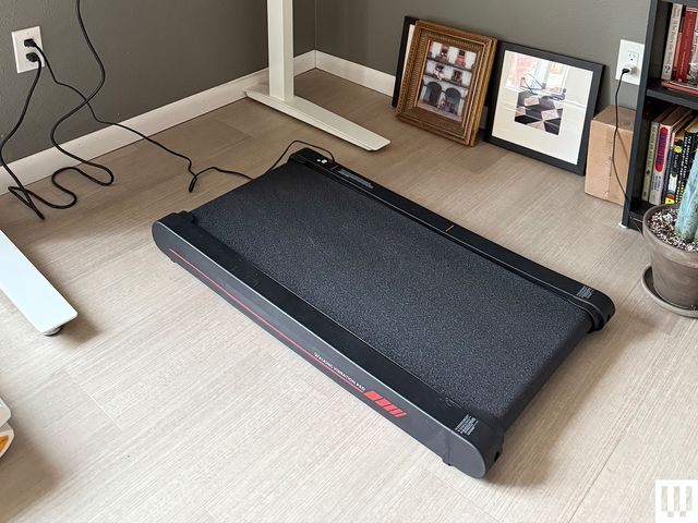 Sperax Walking Pad, a mini treadmill without handlebars, on the floor under a standing desk