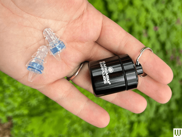 Hand holding small black canister on a keyring and 2 clear ear cushions