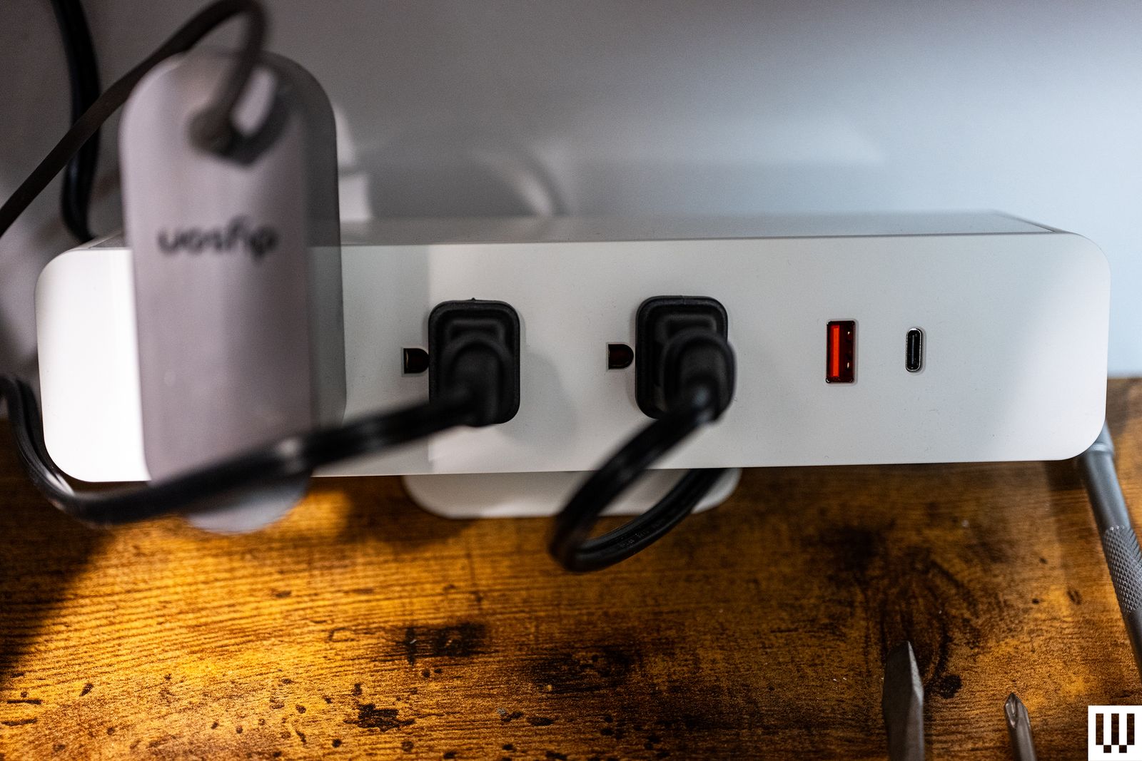Front view of Branch Clamp On a white electrical power strip gripping the edge of a wooden desk
