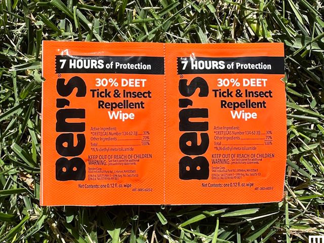 Ben’s Tick and Insect Repellent Wipes, two orange packets with black lettering, laying in a patch of grass