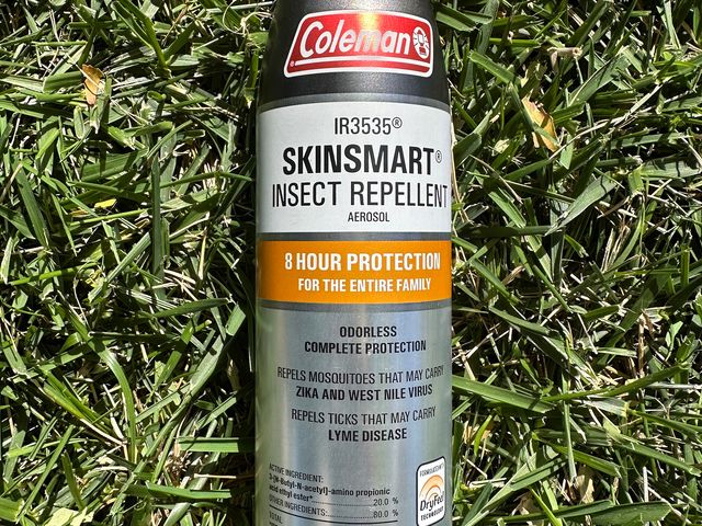 Coleman Insect Repellent Spray, a silver aluminum can with orange cap, laying in a patch of grass