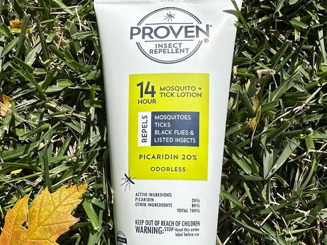 Proven Insect Repellent Lotion, a white squeezable tube, laying on top of a patch of grass with a leaf beside it