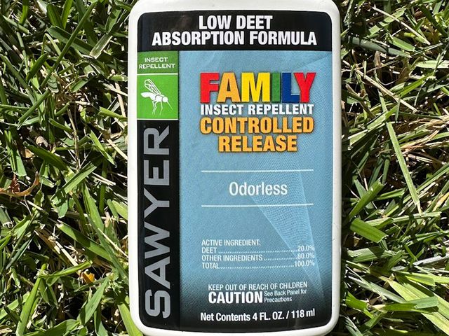 Sawyer 20 Percent DEET Premium Family Insect Repellent Controlled Release, a white bottle with black and blue label, laying in a patch of grass