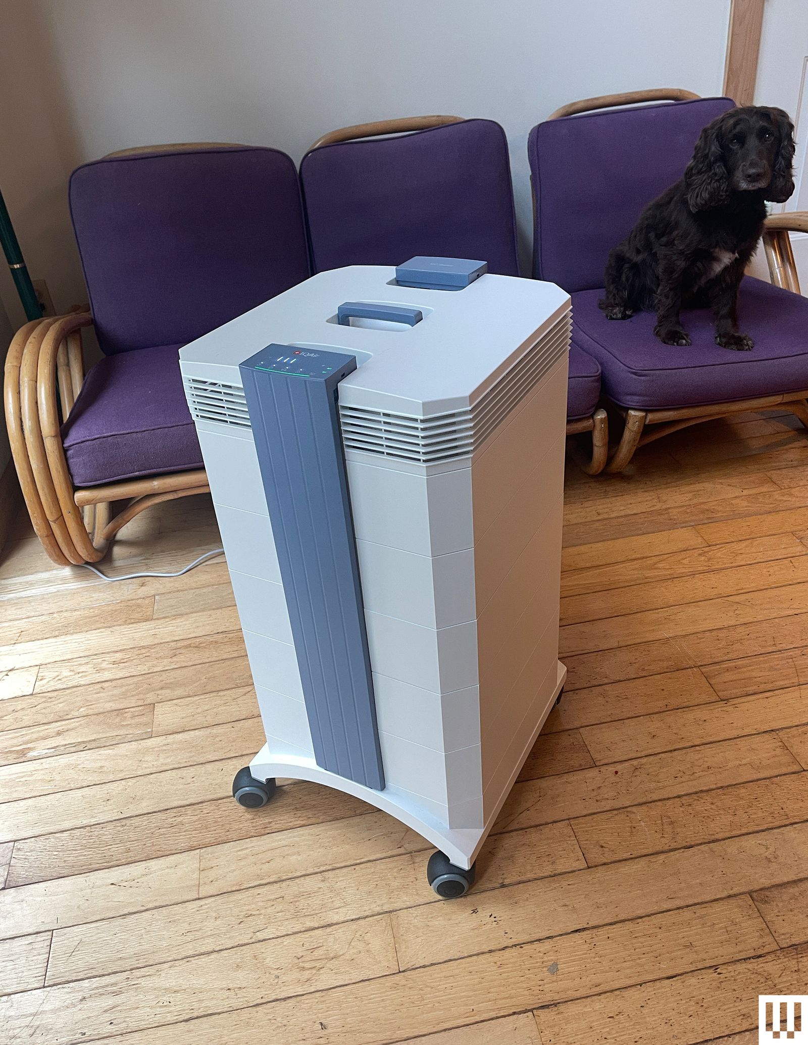 Tall white rectangular air purifier on wheels with 3 purple chairs behind it