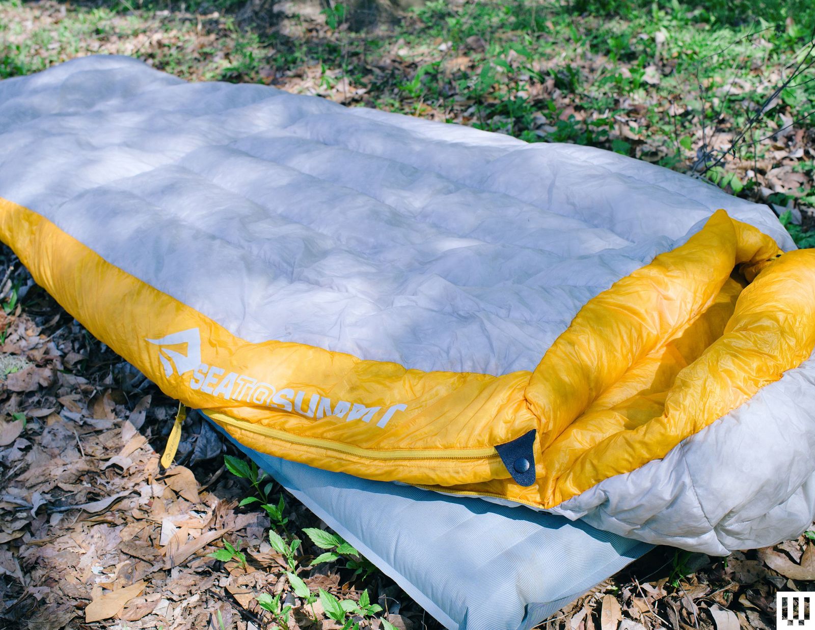 Grey and yellow sleeping bag on top of an inflatable sleeping pad both on the grass